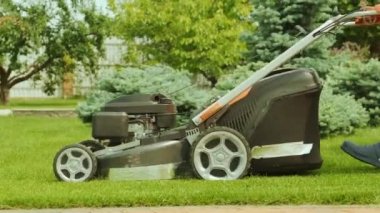 Çim biçme makinesi çimleri kesiyor. Bahçe işleri. Güneşli bahçede çim biçme makinesiyle çimleri biçmek. Bahçede çim biçme makinesiyle çalışan bahçıvan. Çim biçme makinesi yeşil çimleri kesiyor