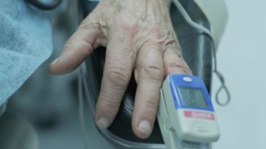 Hastanede ameliyat sırasında parmak üzerinde nabız oksimetresi olan eski bir hasta.