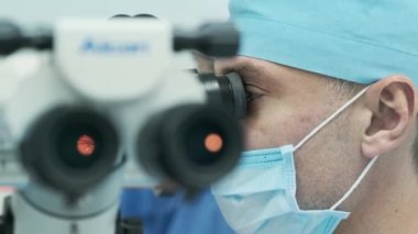 Cerrah ameliyathanedeki kadın hastanın gözündeki mikroskopu inceliyor. Göz ameliyatı sırasında mikroskop kullanan doktor katarakt ve diyopter düzeltmesi yapıyor..