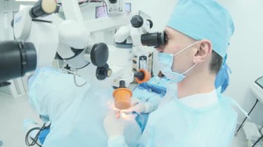 Cerrah ameliyathanedeki kadın hastanın gözündeki mikroskopu inceliyor. Göz ameliyatı sırasında mikroskop kullanan doktor katarakt ve diyopter düzeltmesi yapıyor..