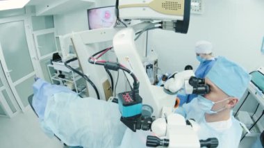Cerrah ameliyathanedeki kadın hastanın gözündeki mikroskopu inceliyor. Göz ameliyatı sırasında mikroskop kullanan doktor katarakt ve diyopter düzeltmesi yapıyor..