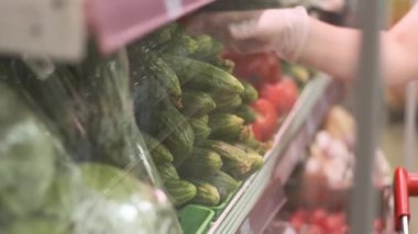 Lastik eldivenli kadın taze salatalıkları topluyor ve bir süpermarkette plastik bir torbaya koyuyor. Coronavirus koruması.