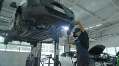 Araba servisi bir arabanın egzoz borusunu kaynaklayıp tamir ediyor. Kaldırılmış bir arabada kaynakçılık işi. Arkadan bak. Tamirci arabanın tabanını kaynaklıyor..