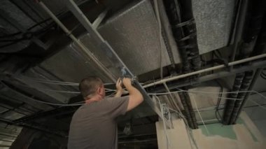 İnşaat işçisi asılmış tavanı alçıpanla birleştiriyor ve alçıpanı tornavidayla tavandaki metal çerçeveye yerleştiriyor. Tadilat, inşaat ve kendin yap..