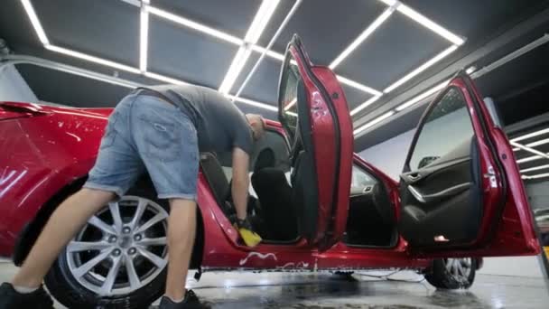 Człowiek Pracownik Myje Czerwony Samochód Myjni Samochodowej Żółtą Ścierką — Wideo stockowe