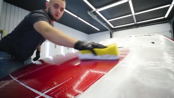 黄色の洗濯布で車の洗浄に赤い車を洗う男の労働者 — ストック動画