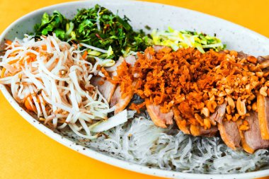 Kavrulmuş kokulu ördek, cam erişteli ve sebze salatası, üzerine kavrulmuş soğan ve fındık seramik tabak serpiştirilmiş, sarı arka planda, Asya yemeği, yakın plan.