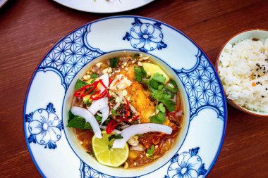 Ekmek kırıntıları, sebze, acı biber, ananas ve hindistan cevizi, tatlı ve ekşi sos, limon, ezilmiş fıstıkla birlikte beyaz tabakta mavi süslemeler, masada pilav. Asya yemeği, yakın plan..