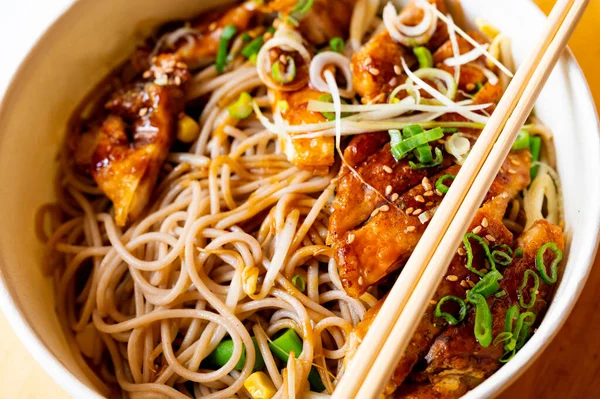 Bowl with soba noodles, chicken meat, green onion, sprouts and sesame seeds with chopsticks, asian (japan) meal. Portion for one person for taking away.