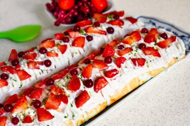 İki çilekli ve üzümlü kek (roulade) masada, içinde meyve ve yeşil mutfak spatulası olan..