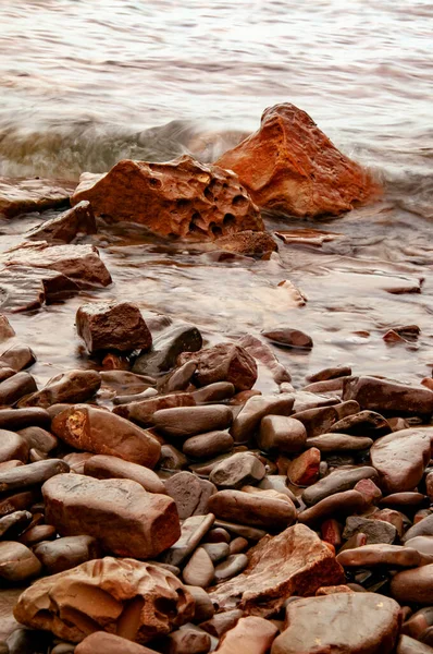 Orange stones and pebbles in sea water with wave.