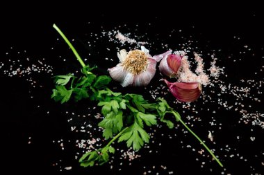 Siyah arkaplanda pembe tuz serpiştirilmiş sarımsak ve maydanoz yaprağı..