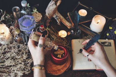 Wiccan cadısı bir büyü yapıyor ve Gölgeler Kitabı 'nın boş sayfalarına yazıyor. Elinde bitki kavanozu ve tüy tutan kadın mihrabında Grimoire yazmaya hazır kurumuş çiçekler, yanan mumlar ve iksirlerle dolu. 