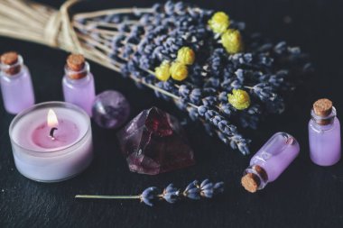 Herbal magick in wicca and witchcraft using lavender infused water. Purple lit burning candle, amethyst pyramid crystal, dried lavender flowers on a black table altar with pastel colored small potion bottles clipart