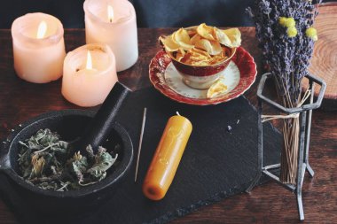 Symbols and sigils carved onto a yellow gold color candlestick, that is laying on a black surface. Witchy elements in a slightly blurred background, like burning candles and dried flowers clipart