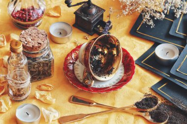 Çay fincanı, çay yapraklarını okumak için bir cadı mihrabında yan yatar. Geleceği haber vermek için bir kehanet olarak. Doğa elementleri ve tarot kartlarıyla fotoğraftaki parlak sarı kumaş.