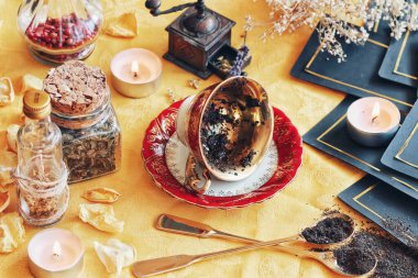 Çay fincanı, çay yapraklarını okumak için bir cadı mihrabında yan yatar. Geleceği haber vermek için bir kehanet olarak. Doğa elementleri ve tarot kartlarıyla fotoğraftaki parlak sarı kumaş.