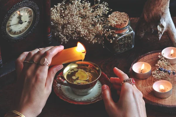 女邪恶女巫戴着老式珠宝 手持黄色的蜡烛 并将蜡倒入红色的金色茶杯中作为占卜方法 阅读烛光蜡 狂欢节 自然物品中的陶瓷 点燃的蜡烛 — 图库照片