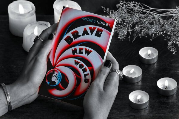 Brussels, Belgium - May 23rd, 2020: Aldous Huxley book Brave New World in dark and sad black and white color pallet with the book itself saturated and colorful. Vintage book is held in female's hands.