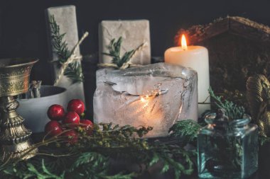 Buzda yanan bir mumun yanına. Noel şenlikli Noel gündönümü (Noel) cadı sunağı üzerine kurulmuştur, her yeşillik, hediye, hediye, beyaz yanan mum, altın tütsü yakıcı, kırmızı kutsal çilek gibi doğa eşyalarıyla doludur.