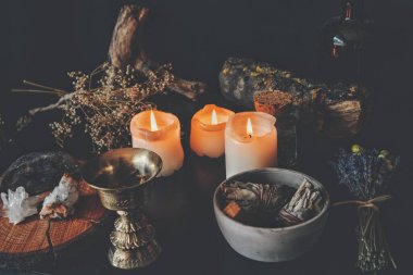 Wiccan cadı sunağı, bir büyü için malzemelerle dolu dağınık çalışma alanı. Kurumuş bitkiler doğa elementleri dallar ve lavanta yanan mumlar, adaçayı rengi çubuklar ve altın rengi tütsü tutacağı olan bir masada.