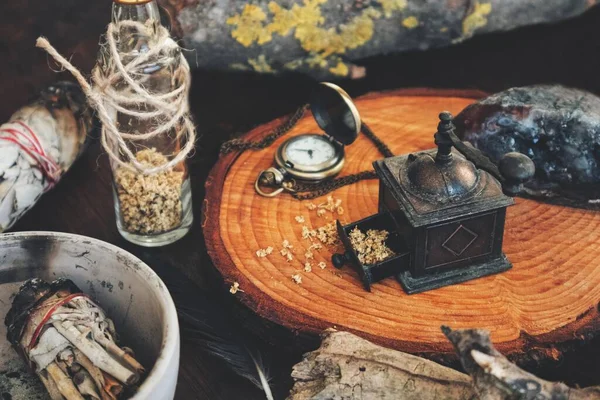 Close up of a mess in a witch\'s kitchen. Wiccan with altar filled with sage smudge sticks, dried herbs, bottles, crystals, tree barks. Messy work space after spell casting on black table background