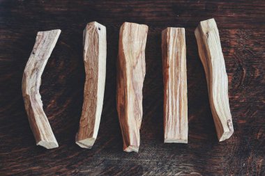 Palo Santo 'nun düz yatağı, Bursera mezarlıklarından (kutsal ağaç) koyu kahverengi ahşap masa üzerine serilmiş. Tek sıra halinde 5 çubuk ayır. Enerji için duman temizleme çubukları kötü titreşimleri temizler.