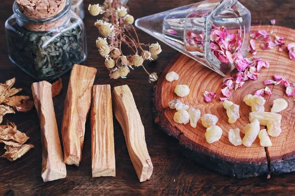 Palo Santo sticks from Bursera graveolens (holy wood) tree on wiccan witch altar, ready for smoke cleansing energy clearing of bad vibes. Nature background with dried herbs flowers, jars, frankincense