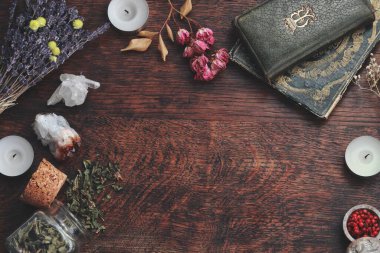 Metinler için koyu kahverengi ahşap masa arkaplanı cadı cadı eşyalarıyla süslenmiş, esrarengiz ve esrarengiz görünsün diye. Ortada bedava yazım alanı var. Kurumuş otlar, kristaller, eski kitaplar, mumlar.