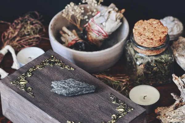 黑色基安石水晶岩石放置在深褐色木制女巫的盒子上 用各种干草 鼠尾草棒 蜡烛包裹在模糊的背景中 肮脏邪恶的女巫祭坛 — 图库照片