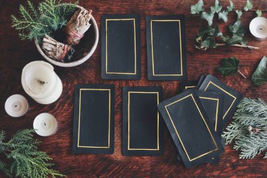 Tarot 4 kartı bir doğa göstergesine (düz yatay) serildi. Her yer yeşillik, sarmaşık, adaçayı lekesi ve beyaz mumlarla çevrili, koyu ahşap bir masada el yapımı tarot kartları. Altın kenarlı siyah kartlar