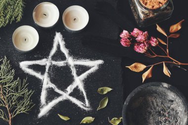 Wiccan cadı sunağında tuz pentagramı sembolü. Cadılık ritüeli için beş köşeli yıldız korunması ve meditasyon. Beyaz mumlar, kurumuş çiçekler, otlar, siyah masa yüzeyinde her yer yeşillik.