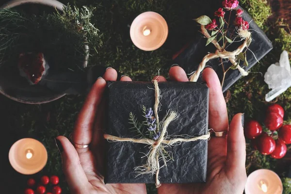 耶勒冬至 圣诞节 主题平平的女性手托着一个用纱线包裹的黑色礼品盒 手里拿着鲜花 森林苔藓 点燃的蜡烛 红色浆果 — 图库照片