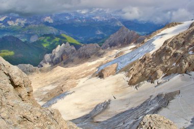 Marmolada zirvesinden görüntü. Buzullu keskin kayalar, arka planda yeşil çayırlar. Bulutlar. Dolomitler Dağları. 