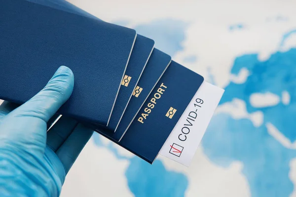 Immunity passport, risk-free certificate concept. Hand in medical gloves holds passports with note COVID-19 and red check mark on world map. Coronavirus outbreak situation, traveling after pandemic
