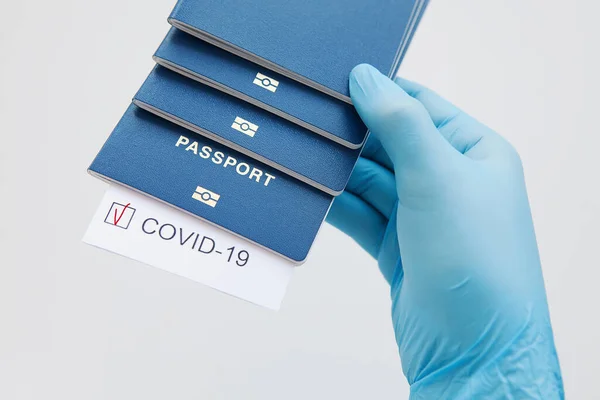 Immunity passport, risk-free certificate concept. Hand in medical glove hold passports with note COVID-19 coronavirus with red check mark. Coronavirus outbreak situation, traveling after pandemic