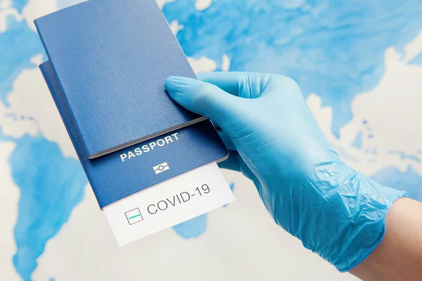 Immunity passport, risk-free certificate concept. Hand in medical gloves holds passports with note COVID-19 and green check mark on world map. Coronavirus outbreak situation, traveling after pandemic concept