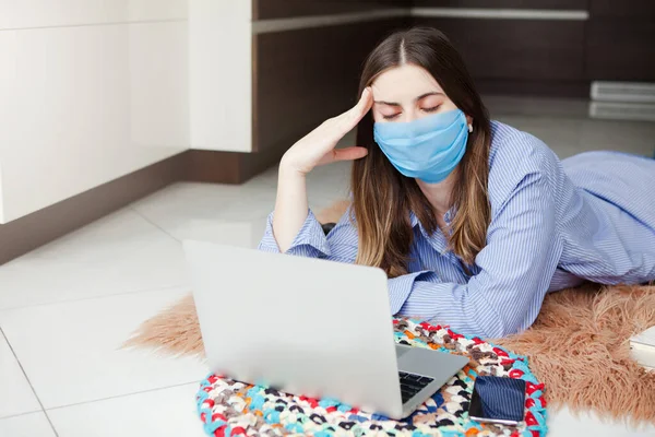 Young woman in medical mask successfully working at home using laptop. Concept home quarantine, isolation, prevention COVID-19, social distancing, freelance work from home office, self-isolation