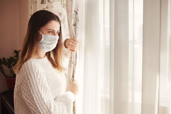 Tıbbi maskeli genç bir kadın kendini karantinaya almak için evde karantinada kalıyor. Ev karantinası, COVID-19 önleme, Coronavirüs salgını durumu