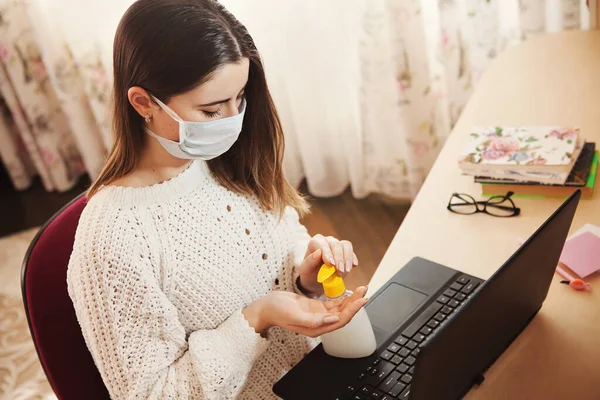 Coronavirus concept. Woman in medical mask working from home. Business woman at home quarantine wearing protective mask. Working from home. Cleaning her hands with sanitizer gel
