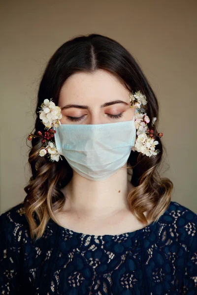 Bahar çiçekleriyle süslenmiş tıbbi maskeli genç ve güzel bir kadın kendini karantinaya almak için evde yalnız kalıyor. Ev karantinası, COVID-19 önleme, Coronavirüs salgını durumu.