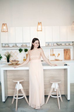 Şık, parlak bir mutfakta, gece elbisesi içinde genç ve güzel bir kadın.