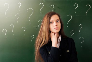 Güzel genç bir kadın tebeşir tahtası ve soru işaretlerinin arka planında duruyor. Eğitim kavramı
