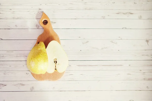 Fresh pear cut in half on pear shaped wooden board on gray wooden background, top view.
