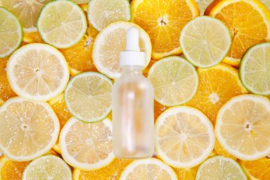 Şeffaf camdan yapılmış bir kozmetik şişesi. Taze limon, portakal ve limon dilimleri üzerine pipetli. Boşluğu kopyala