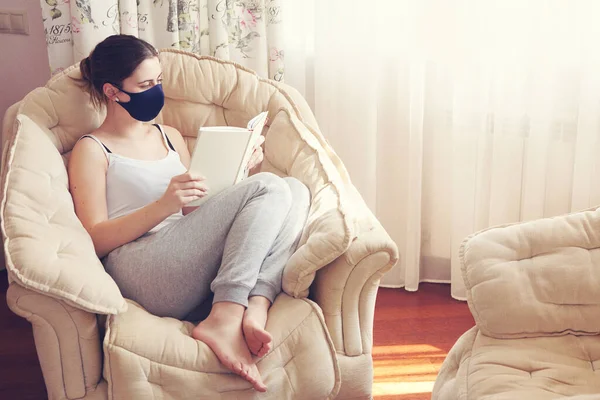 Woman reading book in protective mask, stay isolation at home for self quarantine. Concept home quarantine, prevention COVID-19, Coronavirus outbreak situation