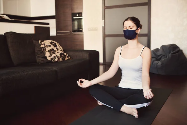 Young woman in protective mask doing yoga, stay isolation at home for self quarantine. Concept home quarantine, prevention COVID-19, Coronavirus outbreak situation, quarantine time with pleasure