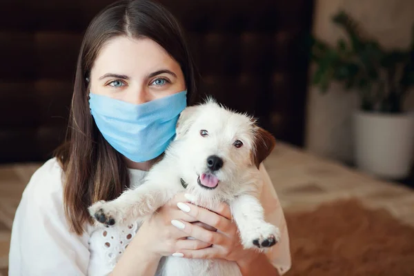 Tıbbi maskeli genç bir kadın ve köpeği Jack Russell Broken evde karantina altında tutuluyorlar. Ev karantinası, COVID-19 önleme, Coronavirüs salgını durumu