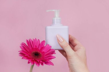 Elinde pembe arka planda narin Gerbera çiçeğiyle kozmetik krema kavanozu var. Boşluğu kopyala