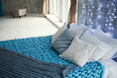 Yastıklar, yatakta örülmüş battaniyeler ve arka planda ampuller. Moda oda tasarımı. Boşluğu kopyala